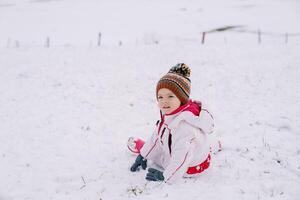 Little smiling girl sits half-turned on the snow photo