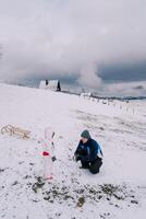 Small child looks at his dad squatting and making a snowball on a hill photo