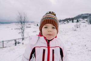 pequeño niña soportes en un cubierto de nieve colina en un montaña Valle foto