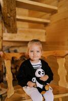 pequeño sonriente niña sentado con suave juguete pandas en un de madera silla en el habitación foto