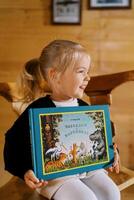 Little smiling girl sits on a chair with a colorful book in her hands. Title. Stories in Pictures photo