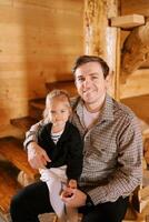 Little girl sitting on smiling dad lap near wooden stairs at home photo