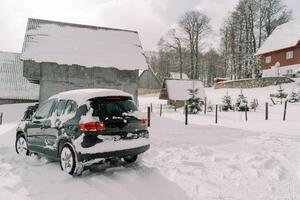 Snow-covered black SUV stands near a cottage in a small village photo