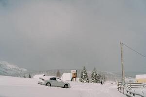 Snow-covered car stands on a hill in a small village in a mountain valley. Side view photo