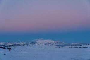 rosado puesta de sol terminado un Nevado montaña Valle foto