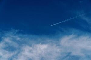 Plane flies in the cloudy sky leaving a trail photo