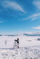 Mom and little girl are making a snowman, standing on a snowy clearing in a mountain valley. Back view photo