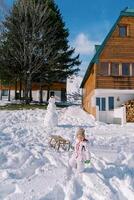 Little girl drags a sled on a rope from a hill near a wooden chalet photo
