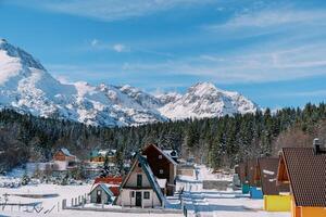 Triangular two-story house in a colorful village at the edge of a coniferous forest in a snowy mountain valley photo