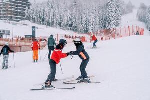 Skiers stand on the mountainside holding hands near those skiing photo