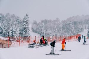Snowmobile with a sleigh rides past skiers on a snow-covered mountain along a red fence photo