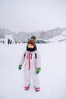 Little smiling girl stands on a snowy ski slope against the backdrop of skiers photo