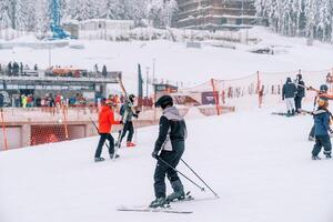 Skiers in helmets go down and up the slope of a snowy mountain photo