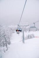 esquiadores en vistoso esquí trajes paseo mediante el nevadas montañas en un telesilla foto