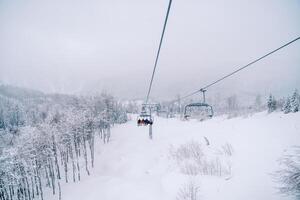 Skiers ride over snow-capped mountains on a four-seater chairlift photo