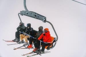 Tourists in ski suits and goggles ride a chairlift up a foggy mountain photo