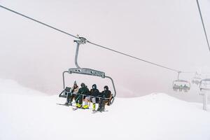People in ski suits on skis ride a chairlift up a foggy snowy slope photo