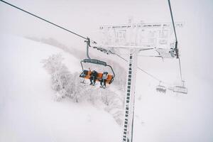 Four-seater chairlift carries skiers up a misty mountain above snow-covered trees photo