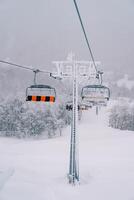 Four-person chairlift seats move along a cable up a snow-covered mountainside photo