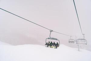 Skiers on chairlift ride up a foggy snowy slope photo