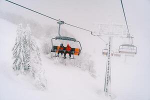 Tourists ride on a ski lift on a foggy mountain above snow-covered trees photo