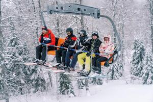 Skiers in bright ski suits ride up a snowy slope on a ski lift photo