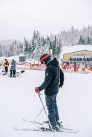 Man in a ski suit stands on skis in the snow and looks at his feet. Side view photo