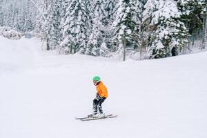 Child in orange ski equipment skis on a snowy slope photo