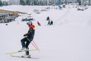hombre en un esquí traje esquís con su pierna doblado a el rodilla en un Nevado Pendiente foto