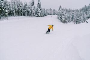 Snowboarder in a yellow ski suit rides a snowboard leaning to the side from a snowy mountain photo