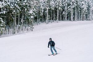 Skier in a ski suit rushes on skis down a snowy slope, leaning to the side photo