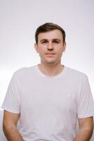 Young serious man in a white T-shirt on a gray background. Portrait photo