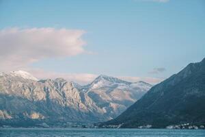 Snow-capped peaks of a high mountain range near the sea in the sun rays photo