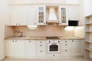 Beige kitchen with white cabinets, hood, stove and sink photo