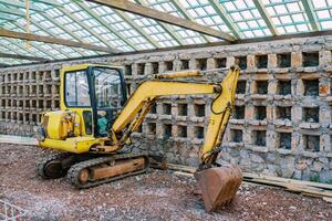 Yellow excavator working in a large brick greenhouse photo