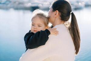 Mother hugs a little girl in her arms while standing by the sea. Back view photo