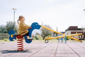 Little girl swings on a spring swing on the playground. Side view photo