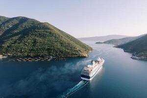 Tall cruise ship sails through the Bay of Kotor along the mountainous coastline. Montenegro. Drone photo