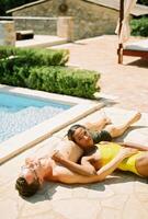 Man sunbathes lying by the pool hugging woman who rests her head on his stomach photo