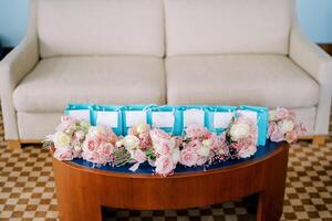 pequeño ramos de flores de rosado rosas mentira en el mesa cerca azul regalo pantalones en el habitación foto