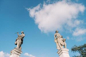 Ancient statues on stone pedestals of the fence of an old villa against a blue sky photo