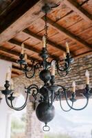 bronce ramificado candelabro con esferas y vela bombillas cuelga desde el de madera techo de un antiguo villa foto