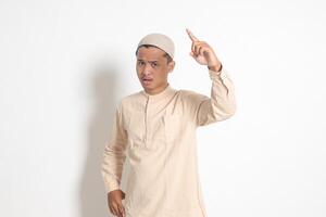 Portrait of attractive Asian muslim man in koko shirt making angry hand gesture with fingers, scolding someone who has done something wrong. Isolated image on white background photo