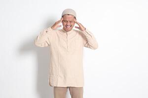 retrato de sufrimiento asiático musulmán hombre en blanco camisa teniendo un migraña, conmovedor su templo. dolor de cabeza enfermedad concepto. aislado imagen en blanco antecedentes foto