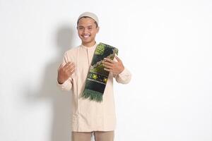 Portrait of attractive Asian muslim man in koko shirt with skullcap inviting and welcoming someone to come in. Isolated image on white background photo