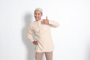 Portrait of attractive Asian muslim man in koko shirt showing thumb up, good job hand gesture. Approval concept. Isolated image on white background photo