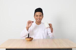 retrato de emocionado asiático musulmán hombre comiendo kurma o fecha Fruta durante sahur y rotura rápido. cultura y tradicion en Ramadán mes. aislado imagen en blanco antecedentes foto