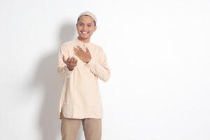 Portrait of attractive Asian muslim man in koko shirt with skullcap inviting and welcoming someone to come in. Isolated image on white background photo