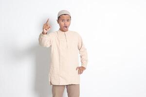Portrait of attractive Asian muslim man in koko shirt making angry hand gesture with fingers, scolding someone who has done something wrong. Isolated image on white background photo