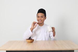 Portrait of excited Asian muslim man eating kurma or date fruit during sahur and breaking fast. Culture and tradition on Ramadan month. Isolated image on white background photo